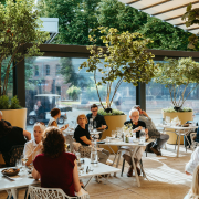 Gäste sitzen auf einer überdachten Terrasse, die Sonne scheint
