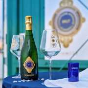 Eine Flasche Champagner Pommery auf einem Stehtisch, sommerlich, im Hintergrund Wasser, zwei Gläser auf dem Tisch