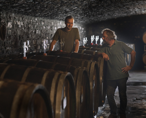 Johannes und Clemens Busch im Keller einer Winzerei, vor Ihnen große Weinfässer